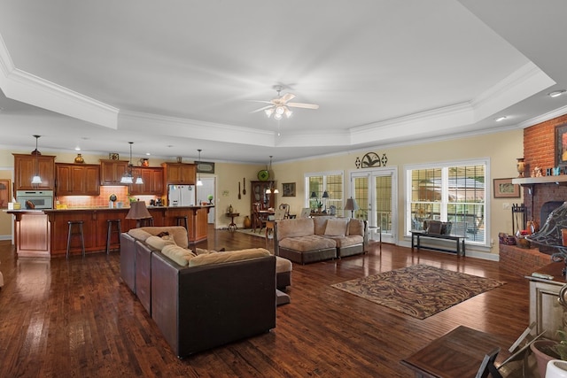 living room featuring a fireplace, ceiling fan, a raised ceiling, crown molding, and dark wood-type flooring