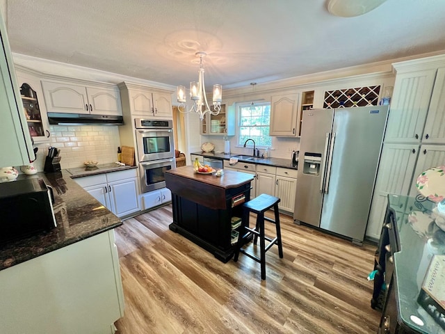 1503 Buena Vista Dr, Dothan, AL 36303 - kitchen with appliances with stainless steel finishes, under cabinet range hood, a chandelier, light wood-style flooring, and decorative backsplash