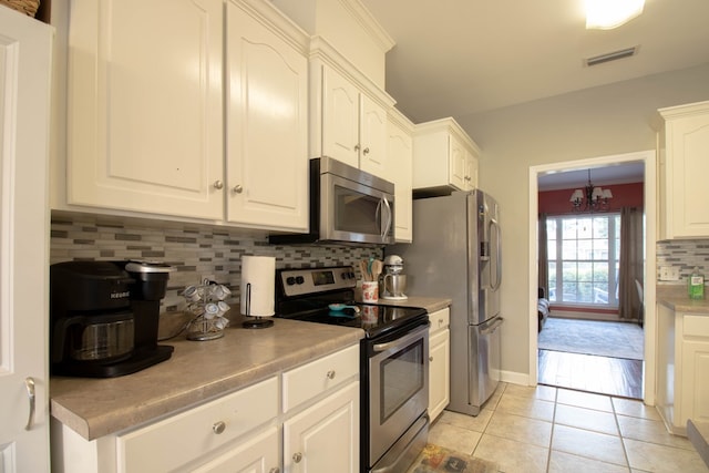 kitchen with white cabinets, decorative backsplash, light tile patterned flooring, stainless steel appliances, and a chandelier