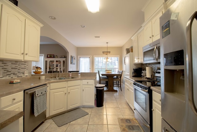 kitchen with pendant lighting, light tile patterned floors, appliances with stainless steel finishes, tasteful backsplash, and kitchen peninsula