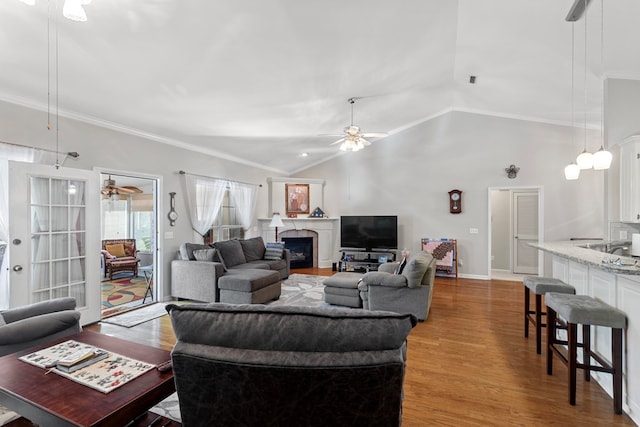 living room with ceiling fan, light wood-type flooring, ornamental molding, and vaulted ceiling