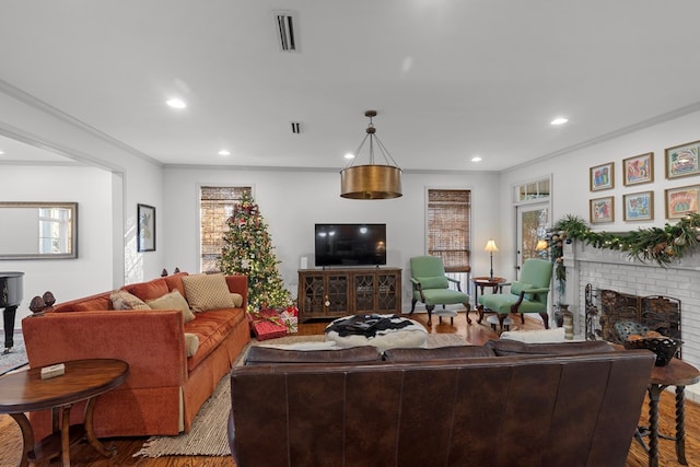 living room with a brick fireplace, a wealth of natural light, crown molding, and hardwood / wood-style flooring