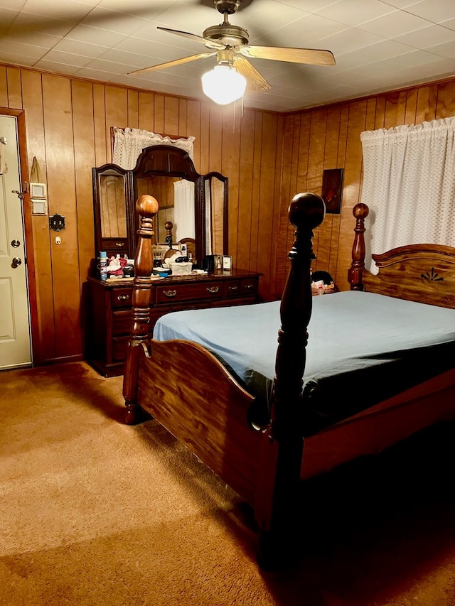 carpeted bedroom featuring ceiling fan and wooden walls