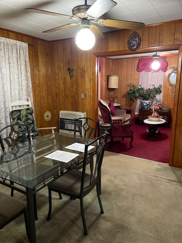 carpeted dining area featuring heating unit, ceiling fan, and wood walls