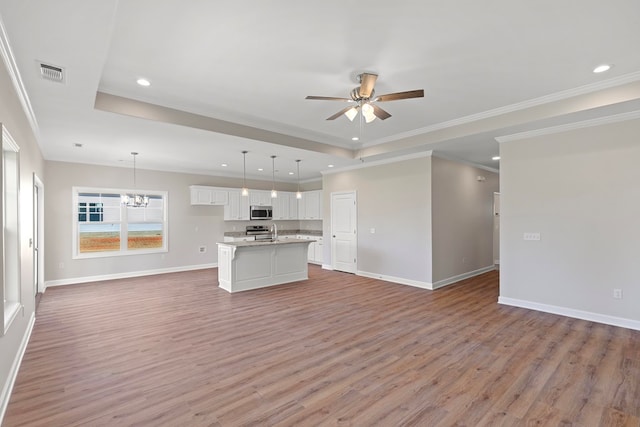 interior space with a tray ceiling, crown molding, wood-type flooring, and ceiling fan with notable chandelier