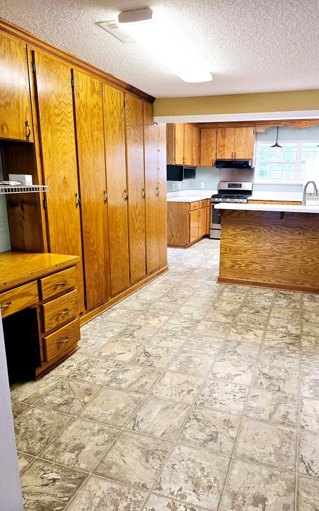 653 Honeysuckle Hills Rd, Ozark, AL 36360 - kitchen featuring stainless steel stove, brown cabinetry, a textured ceiling, light countertops, and under cabinet range hood