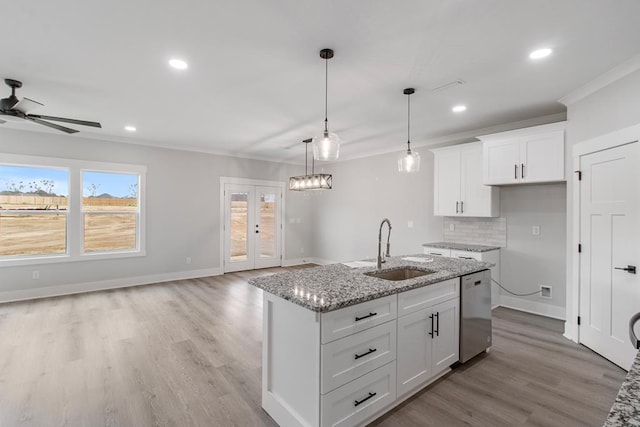 kitchen with light stone counters, a kitchen island with sink, sink, and white cabinets