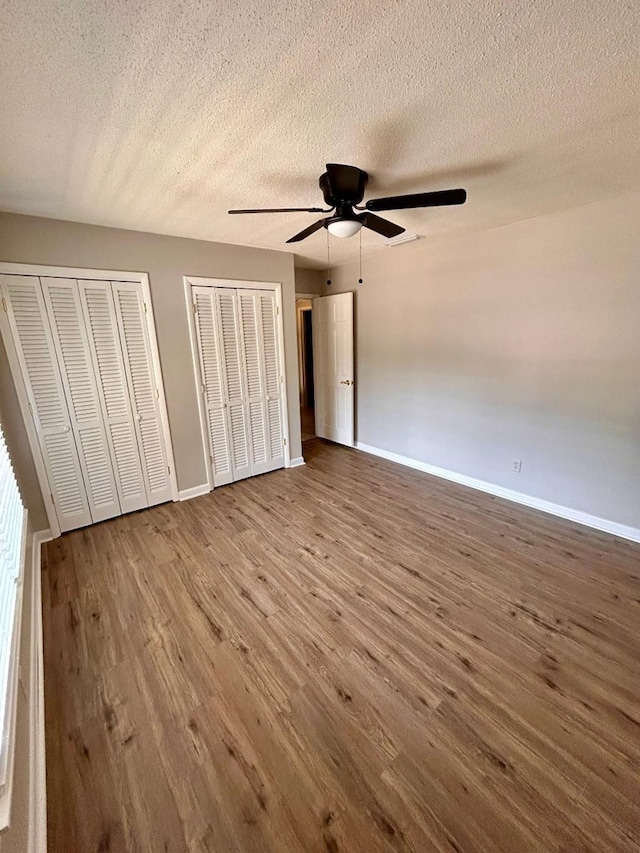 unfurnished bedroom with hardwood / wood-style flooring, ceiling fan, a textured ceiling, and two closets