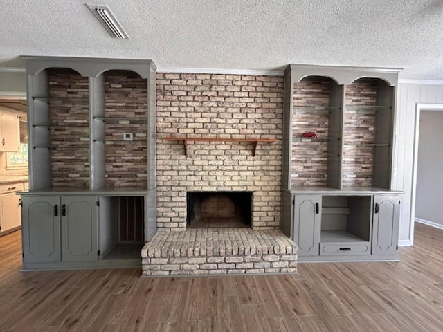 unfurnished living room featuring light hardwood / wood-style floors, a textured ceiling, ornamental molding, and a fireplace