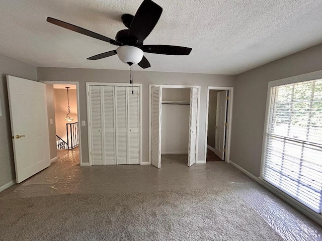 unfurnished bedroom with ceiling fan, multiple closets, and a textured ceiling