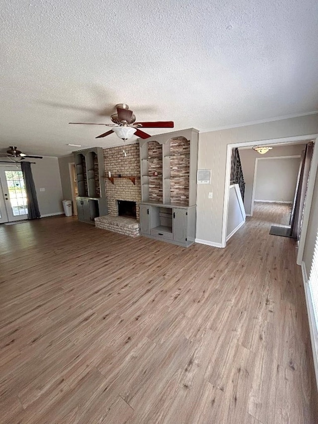 unfurnished living room with light wood-type flooring, a brick fireplace, a textured ceiling, and ceiling fan