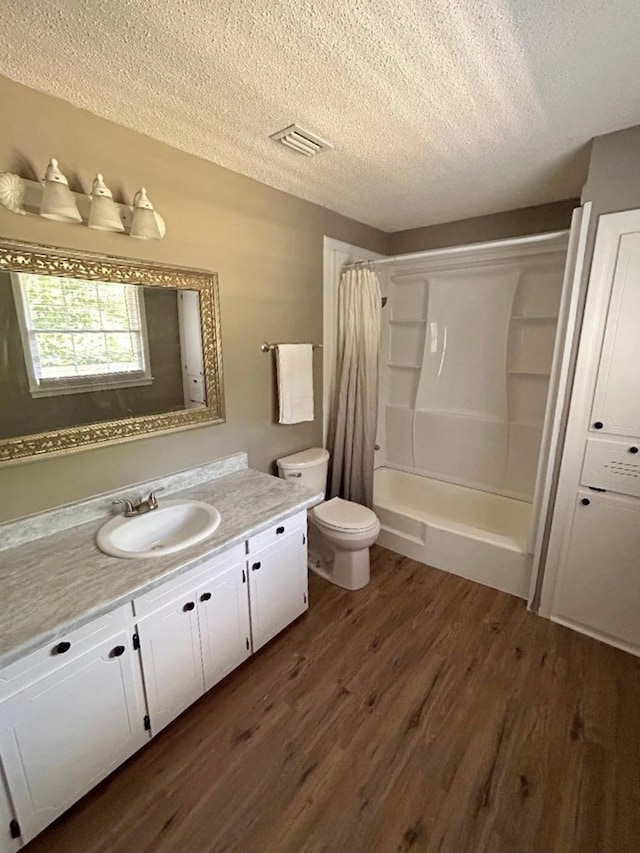 full bathroom featuring hardwood / wood-style floors, shower / bath combo with shower curtain, vanity, a textured ceiling, and toilet