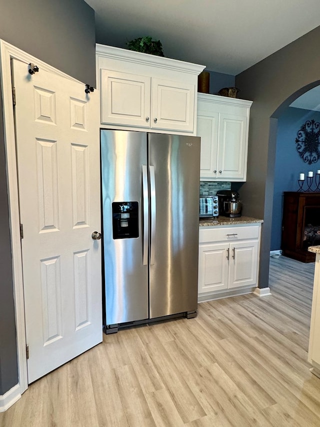 kitchen with white cabinets, arched walkways, stainless steel fridge, and light wood-style floors