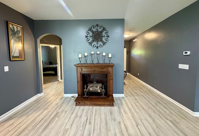 living room featuring arched walkways, wood finished floors, a fireplace with raised hearth, and baseboards
