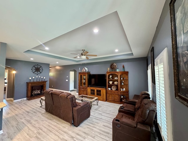 living room featuring arched walkways, a raised ceiling, and light wood-style flooring