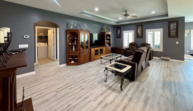 living area with a raised ceiling, arched walkways, light wood-type flooring, ceiling fan, and washer / clothes dryer