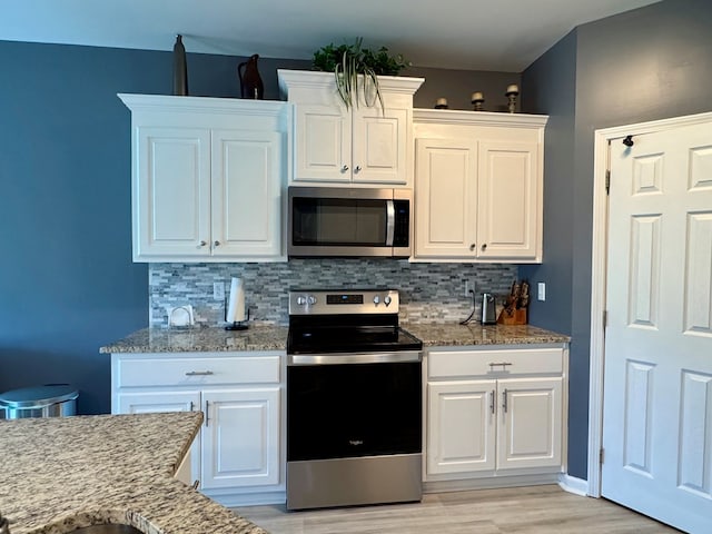 kitchen with white cabinets, decorative backsplash, light wood finished floors, and stainless steel appliances
