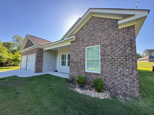 view of side of property with an attached garage, brick siding, a yard, and driveway