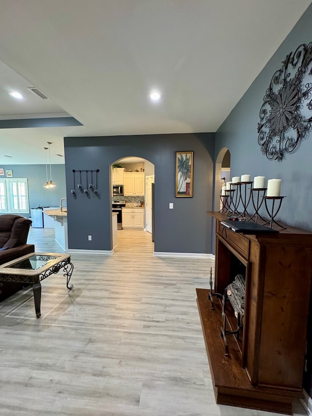 interior space with arched walkways, light wood finished floors, baseboards, visible vents, and recessed lighting