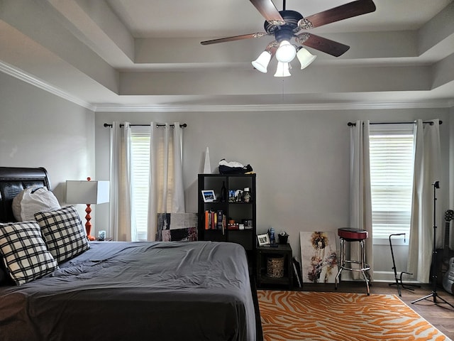 bedroom with a ceiling fan, a tray ceiling, multiple windows, and wood finished floors