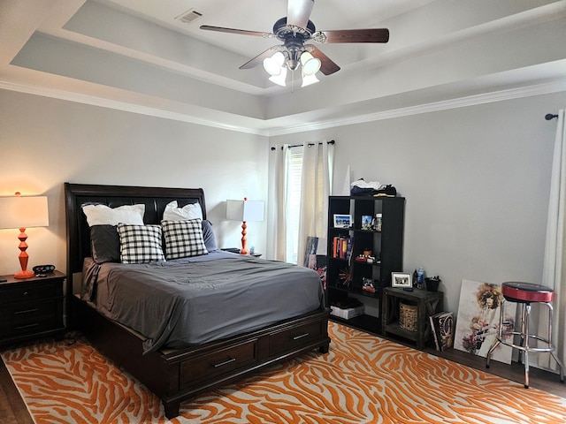 bedroom with a ceiling fan, visible vents, crown molding, wood finished floors, and a tray ceiling