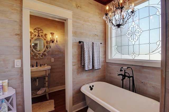 bathroom with wooden walls, sink, hardwood / wood-style flooring, a notable chandelier, and a tub