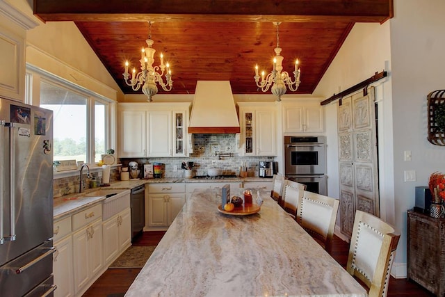 kitchen with decorative light fixtures, a barn door, custom range hood, and stainless steel appliances