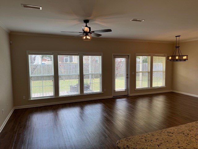 unfurnished room featuring plenty of natural light, ornamental molding, dark wood-type flooring, and ceiling fan with notable chandelier