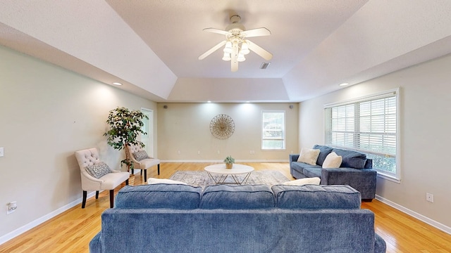 living area with light wood-style flooring, visible vents, a raised ceiling, ceiling fan, and baseboards