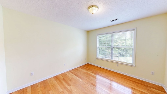 spare room with baseboards, visible vents, a textured ceiling, and light wood finished floors