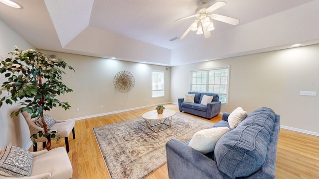 living room with a raised ceiling, ceiling fan, light wood-type flooring, and visible vents