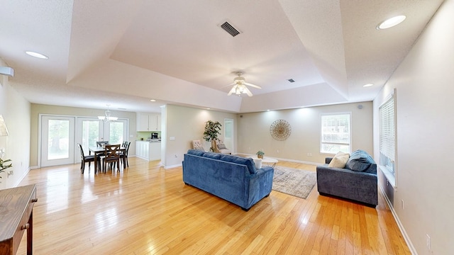 living area featuring ceiling fan with notable chandelier, visible vents, a raised ceiling, and light wood-type flooring