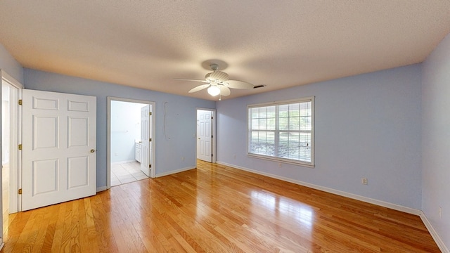 unfurnished bedroom featuring ensuite bathroom, baseboards, light wood-type flooring, a ceiling fan, and a textured ceiling