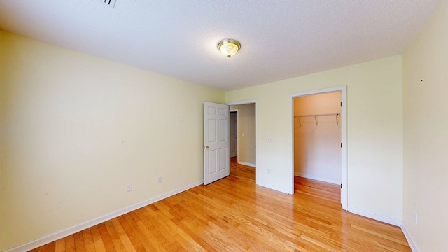 unfurnished bedroom featuring baseboards, a spacious closet, a closet, and light wood-style flooring