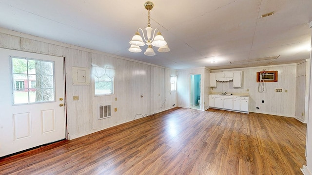 foyer entrance featuring an inviting chandelier, a wall mounted AC, visible vents, wood walls, and wood finished floors