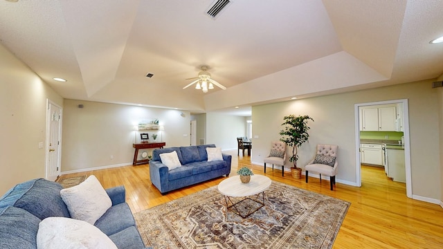 living room with a raised ceiling, a ceiling fan, visible vents, light wood-style flooring, and baseboards