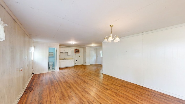 unfurnished living room with wood walls, a notable chandelier, light wood finished floors, and a sink
