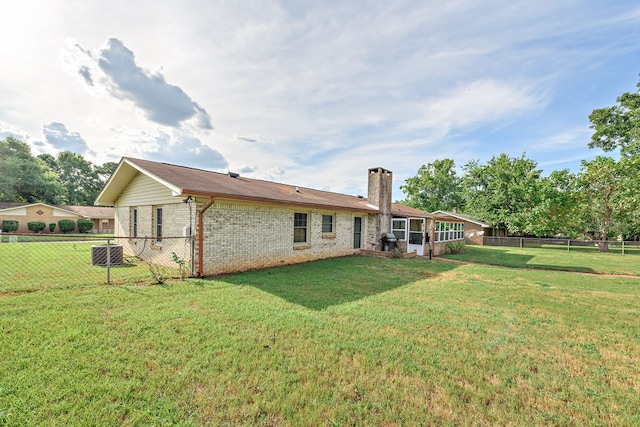 back of house featuring a fenced backyard, central AC, brick siding, a lawn, and a chimney