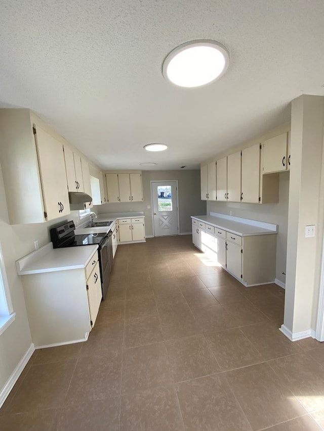 kitchen featuring black range with electric stovetop, sink, dark tile patterned floors, cream cabinets, and a textured ceiling