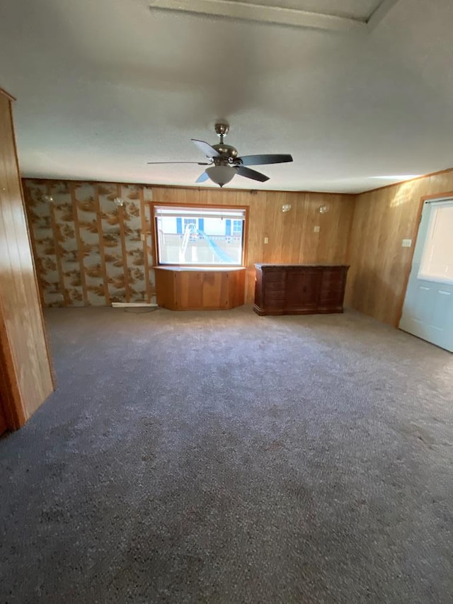 unfurnished living room featuring carpet, ceiling fan, and wood walls