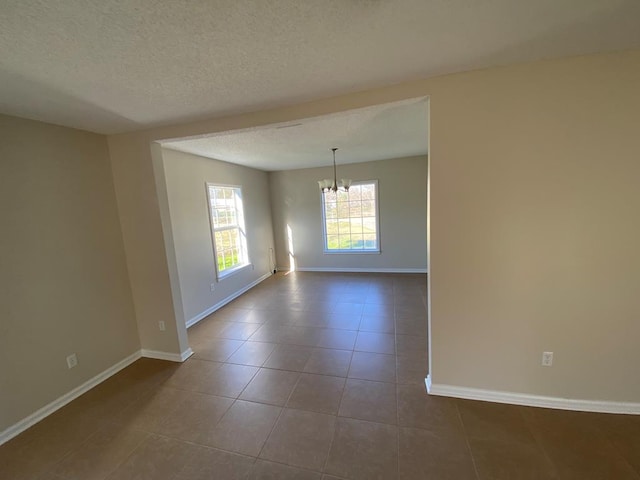 spare room with tile patterned flooring, a textured ceiling, and an inviting chandelier