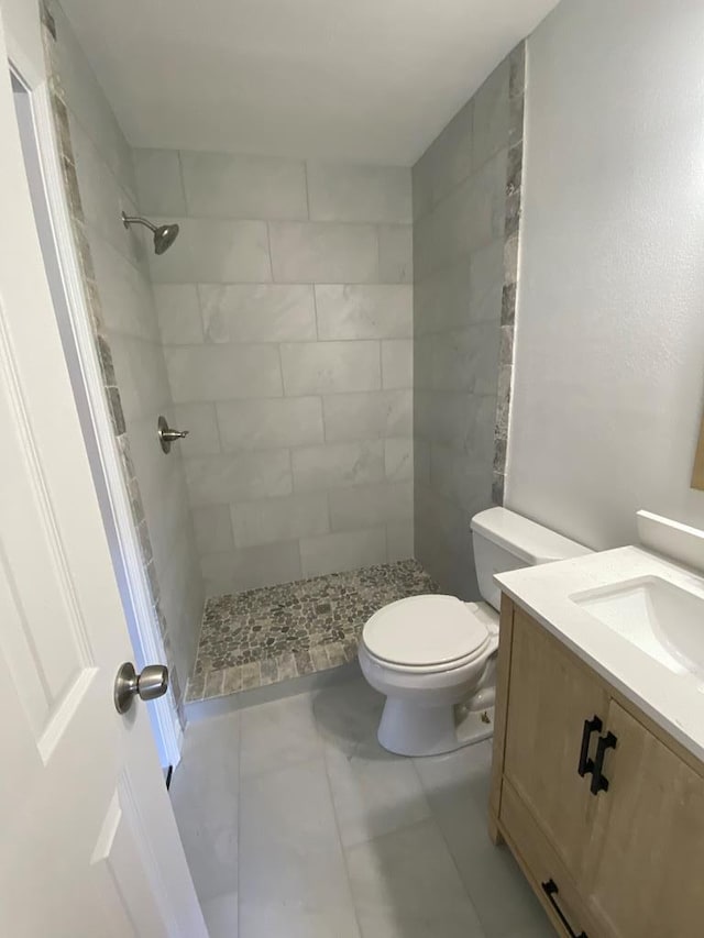 bathroom with a tile shower, vanity, and toilet