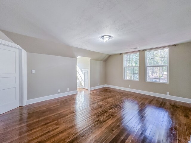 bonus room with lofted ceiling, dark wood-type flooring, and a textured ceiling