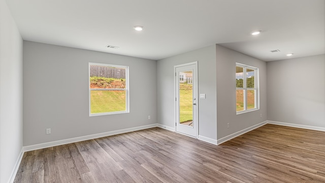 empty room with plenty of natural light, wood finished floors, visible vents, and baseboards