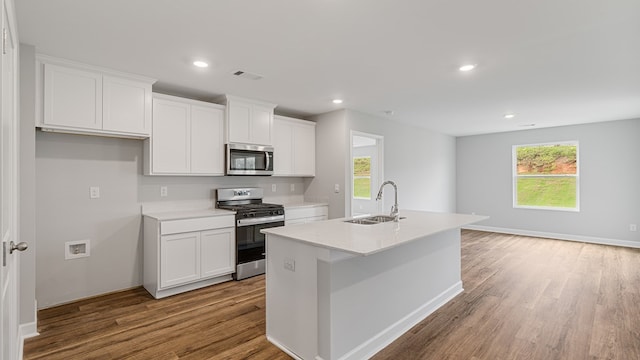 kitchen with a kitchen island with sink, stainless steel appliances, wood finished floors, a sink, and white cabinets