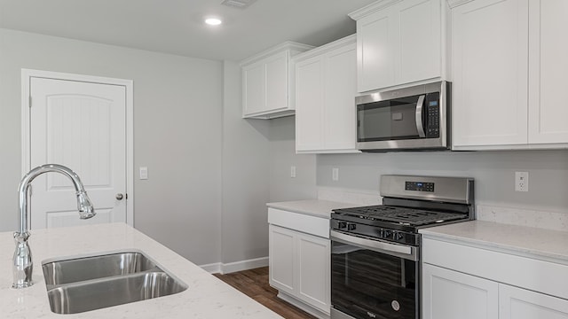 kitchen featuring light stone counters, stainless steel appliances, dark wood-type flooring, white cabinetry, and a sink