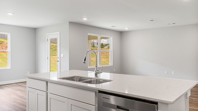 kitchen featuring a kitchen island with sink, light wood-style flooring, a sink, light stone countertops, and dishwasher