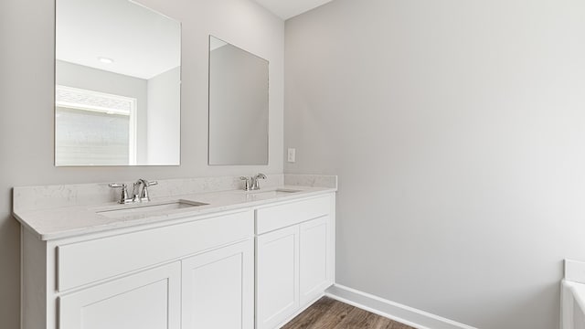 full bathroom featuring double vanity, wood finished floors, a sink, and baseboards