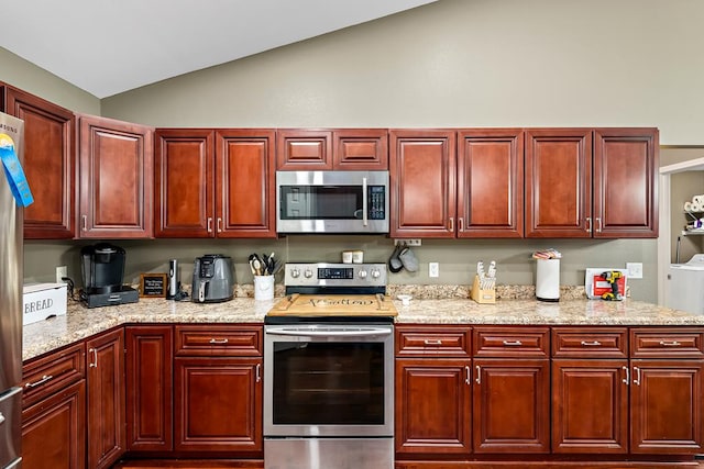 kitchen featuring reddish brown cabinets, appliances with stainless steel finishes, vaulted ceiling, and light stone countertops