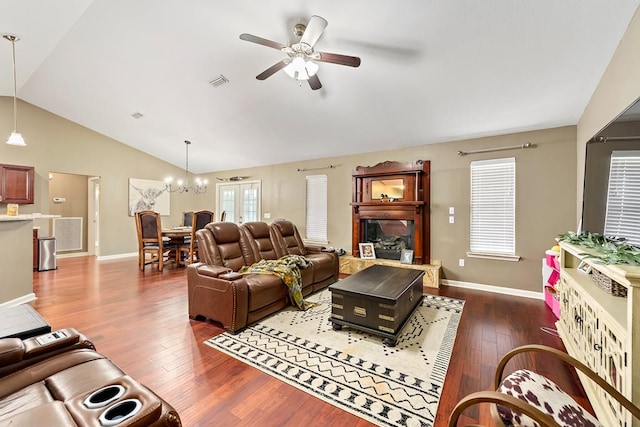 living area featuring ceiling fan with notable chandelier, visible vents, vaulted ceiling, wood finished floors, and baseboards